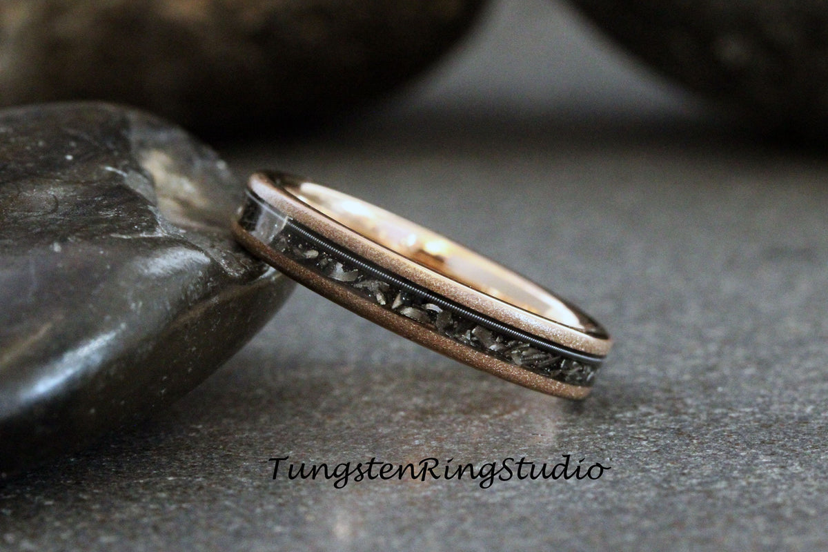 May include: A rose gold tungsten carbide ring with a black inlay. The inlay has a textured pattern.