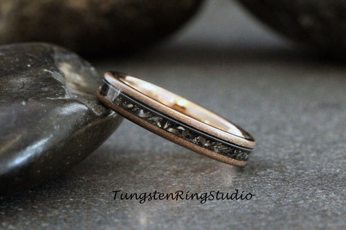 May include: A rose gold tungsten carbide ring with a black inlay. The inlay has a textured pattern.