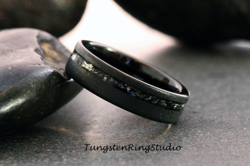 May include: A black tungsten carbide ring with a black inlay and a silver band. The ring is on a gray surface.