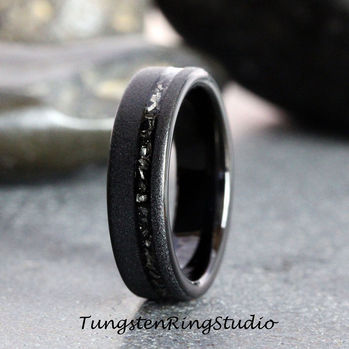 May include: A black tungsten carbide ring with a black diamond inlay. The ring has a brushed finish and a beveled edge.