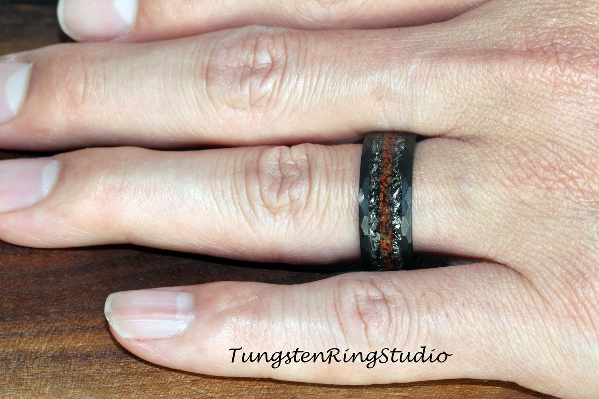 May include: A black tungsten carbide ring with a hammered finish and a red and black inlay. The ring is worn on a person's finger.