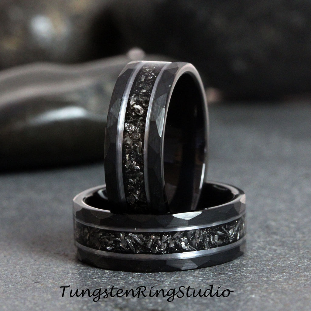 May include: Two black tungsten carbide rings with a hammered finish and a silver inlay. The rings have a textured surface and a beveled edge.