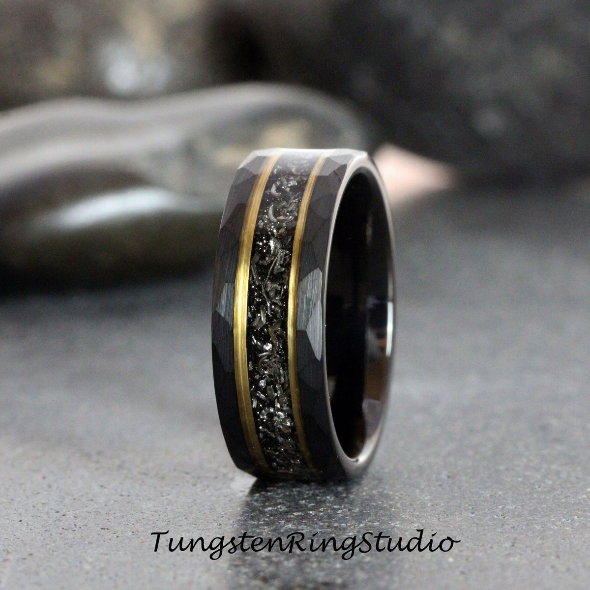 May include: A black tungsten carbide ring with a hammered finish and two gold bands. The ring has a black and silver inlay.