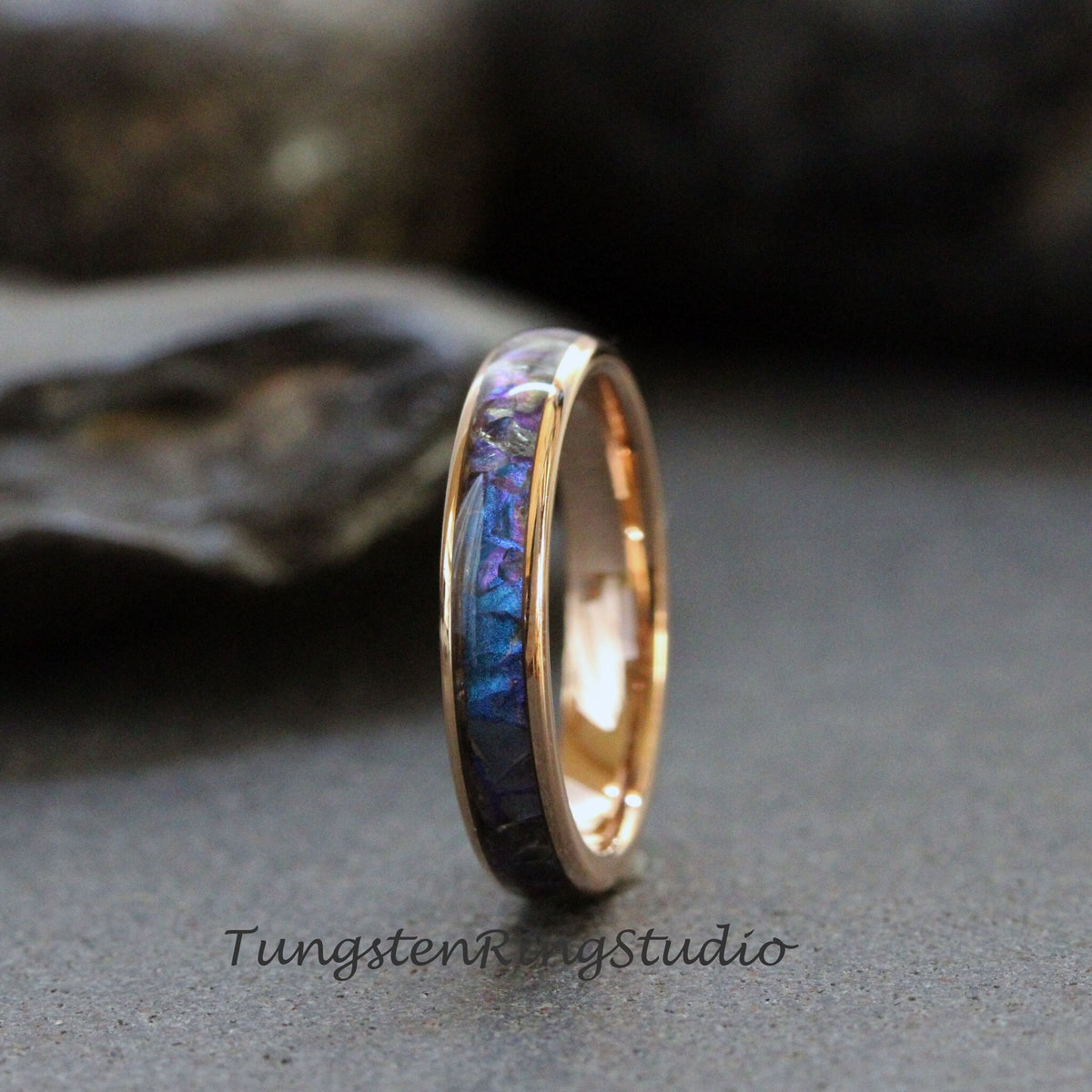 May include: A rose gold tungsten carbide ring with a blue and purple inlay. The inlay is made of crushed meteorite and is set in a polished ring band.