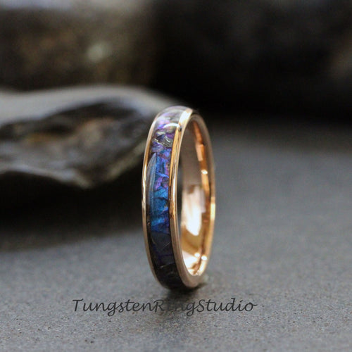 May include: A rose gold tungsten carbide ring with a blue and purple inlay. The inlay is made of crushed meteorite and is set in a polished ring band.