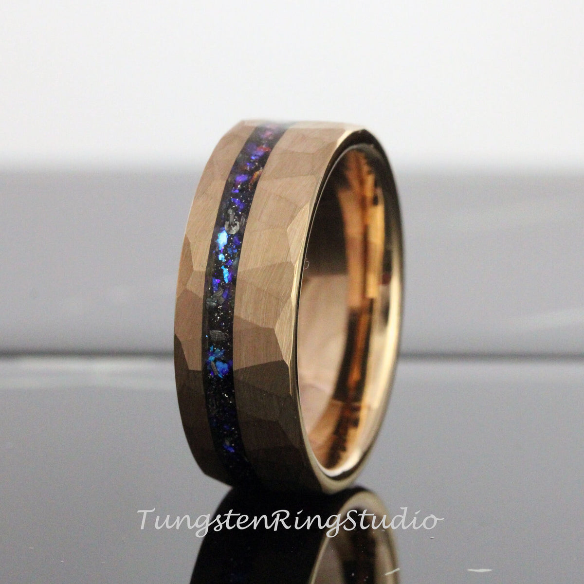 May include: A gold tungsten carbide ring with a hammered finish and a blue and black inlay. The ring is approximately 8mm wide.