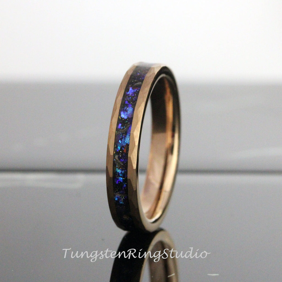 May include: A rose gold tungsten carbide ring with a blue and black inlay. The ring has a hammered finish.