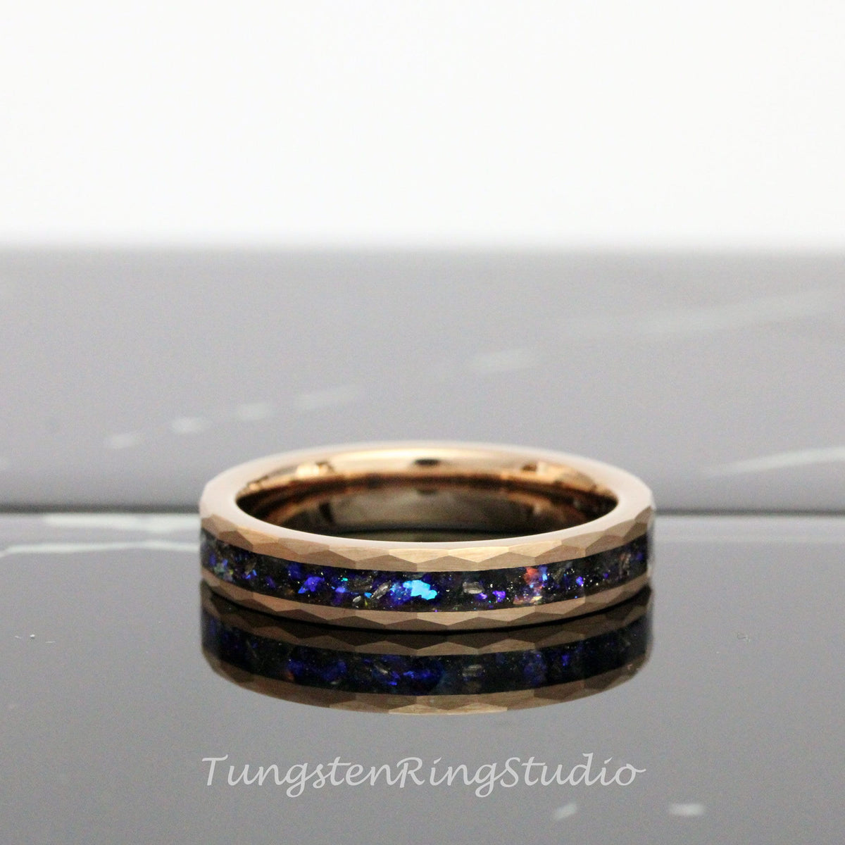 May include: A rose gold tungsten carbide ring with a black and blue inlay. The ring has a beveled edge and a polished finish.