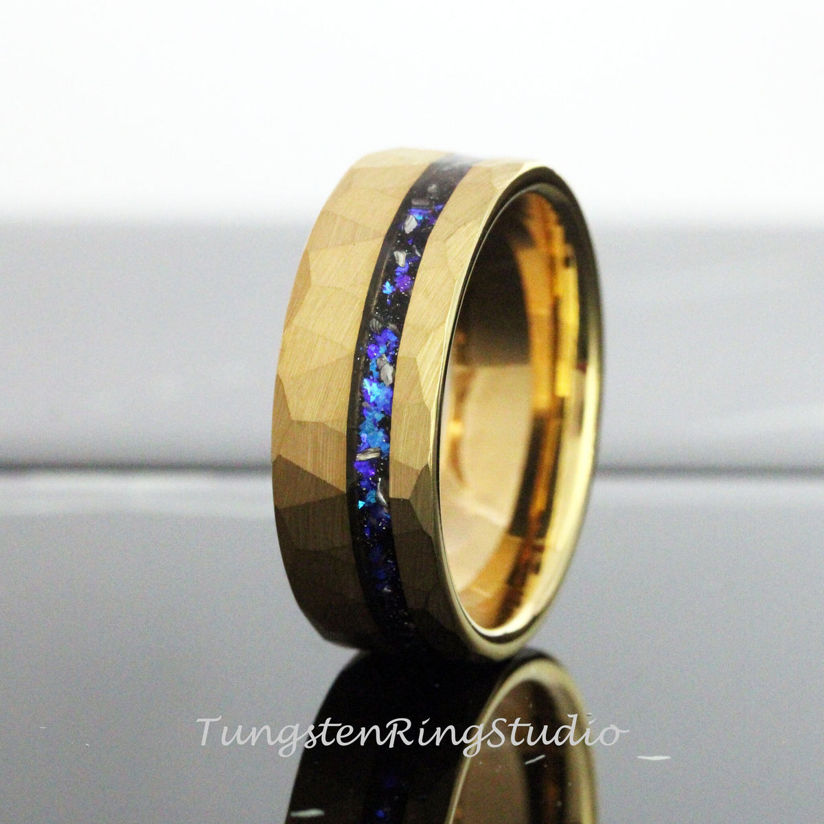 May include: A gold tungsten carbide ring with a hammered finish and a blue and black inlay. The ring is a popular choice for wedding bands.