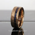 May include: A rose gold tungsten carbide ring with a hammered finish and a blue and black inlay. The ring is approximately 8mm wide.