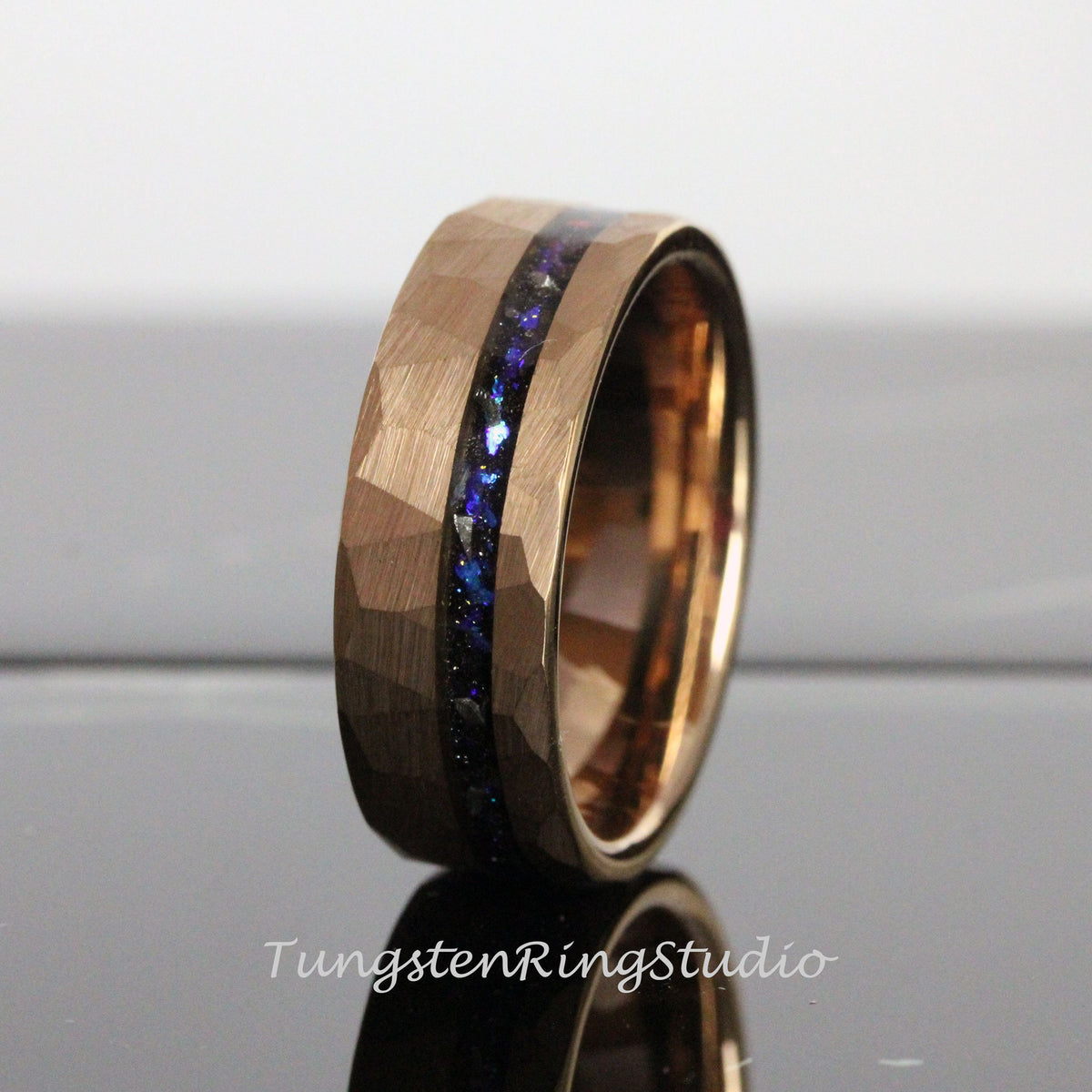 May include: A rose gold tungsten carbide ring with a hammered finish and a blue and black inlay. The ring is approximately 8mm wide.