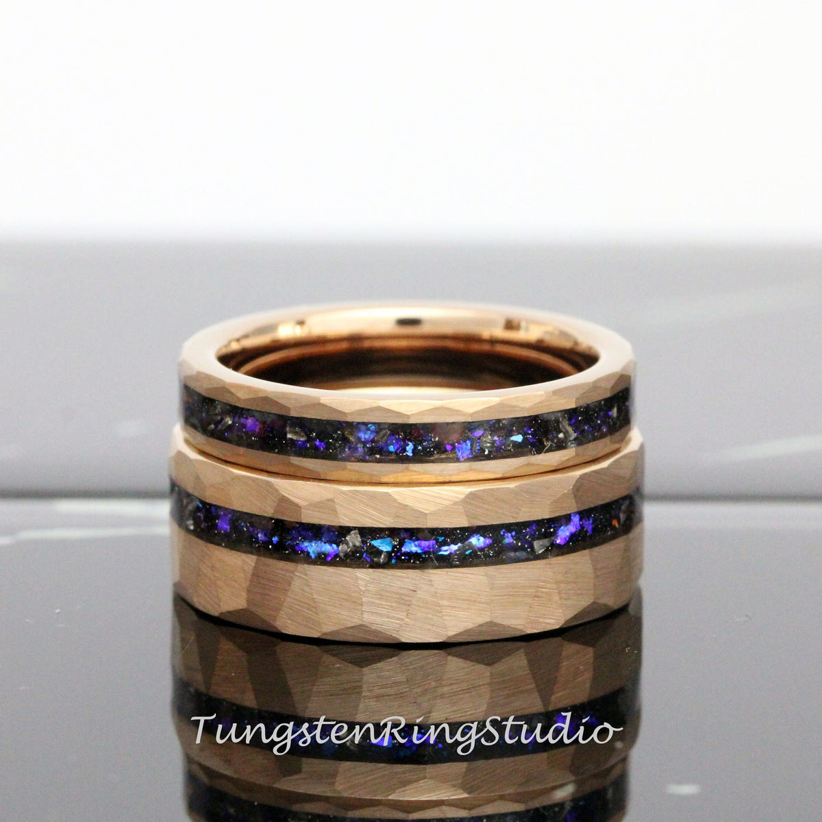 May include: Two gold tungsten carbide rings with a hammered finish and a thin band of iridescent blue and black inlay.