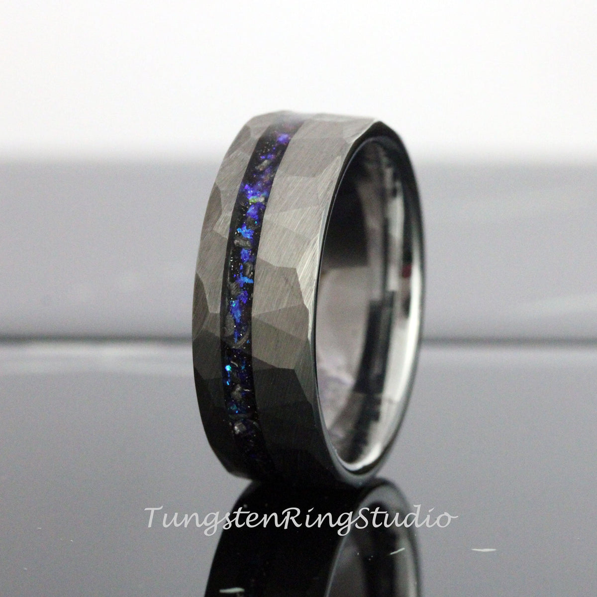 May include: A black tungsten carbide ring with a hammered finish and a blue and black inlay. The ring is a popular choice for men's wedding bands.
