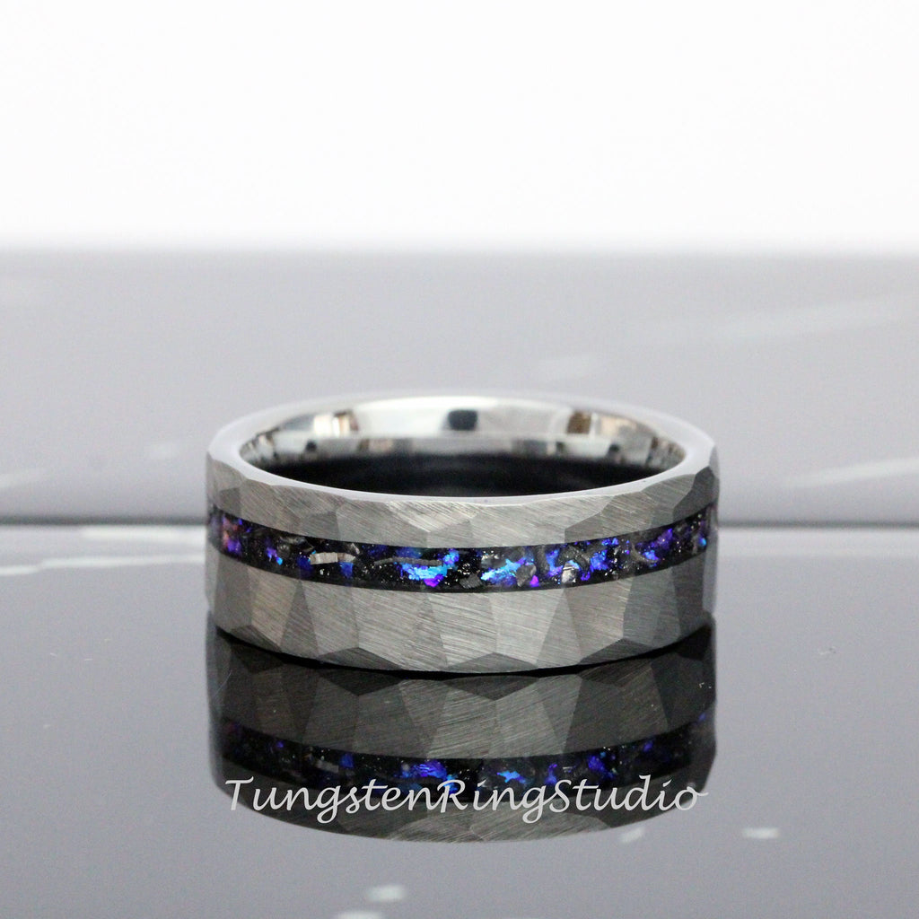 May include: A silver tungsten carbide ring with a hammered finish and a black and blue inlay. The inlay is made of meteorite and opal.