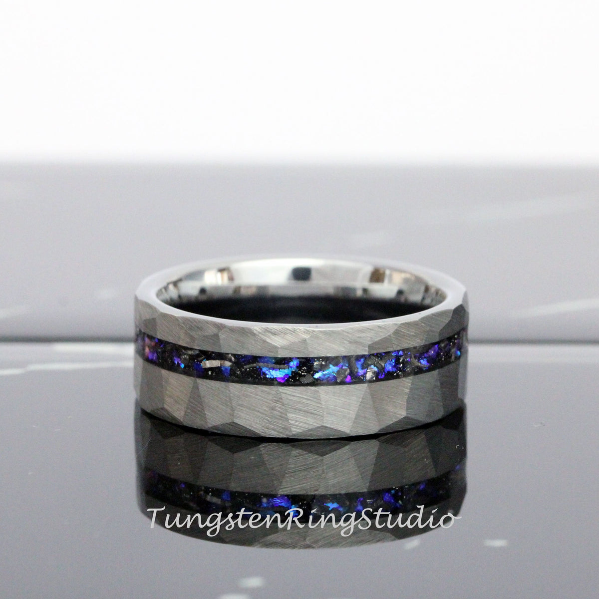 May include: A silver tungsten carbide ring with a hammered finish and a black and blue inlay. The inlay is made of meteorite and opal.