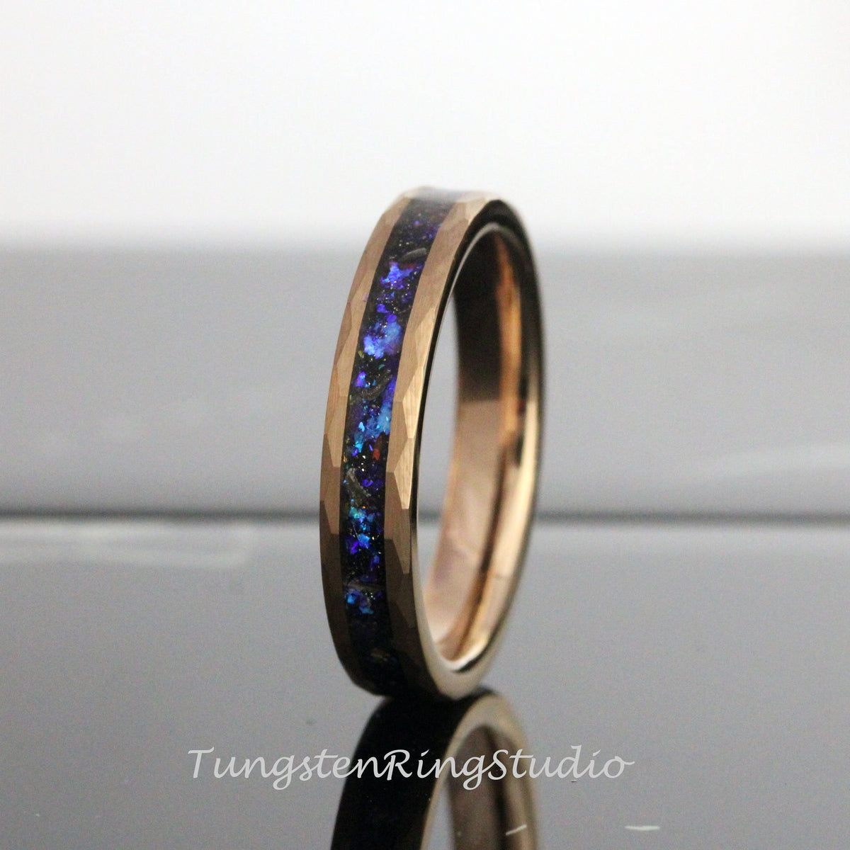 May include: A rose gold tungsten carbide ring with a blue and black inlay. The ring has a hammered finish.