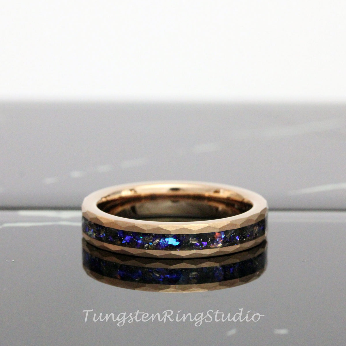 May include: A rose gold tungsten carbide ring with a black and blue inlay. The ring has a beveled edge and a polished finish.