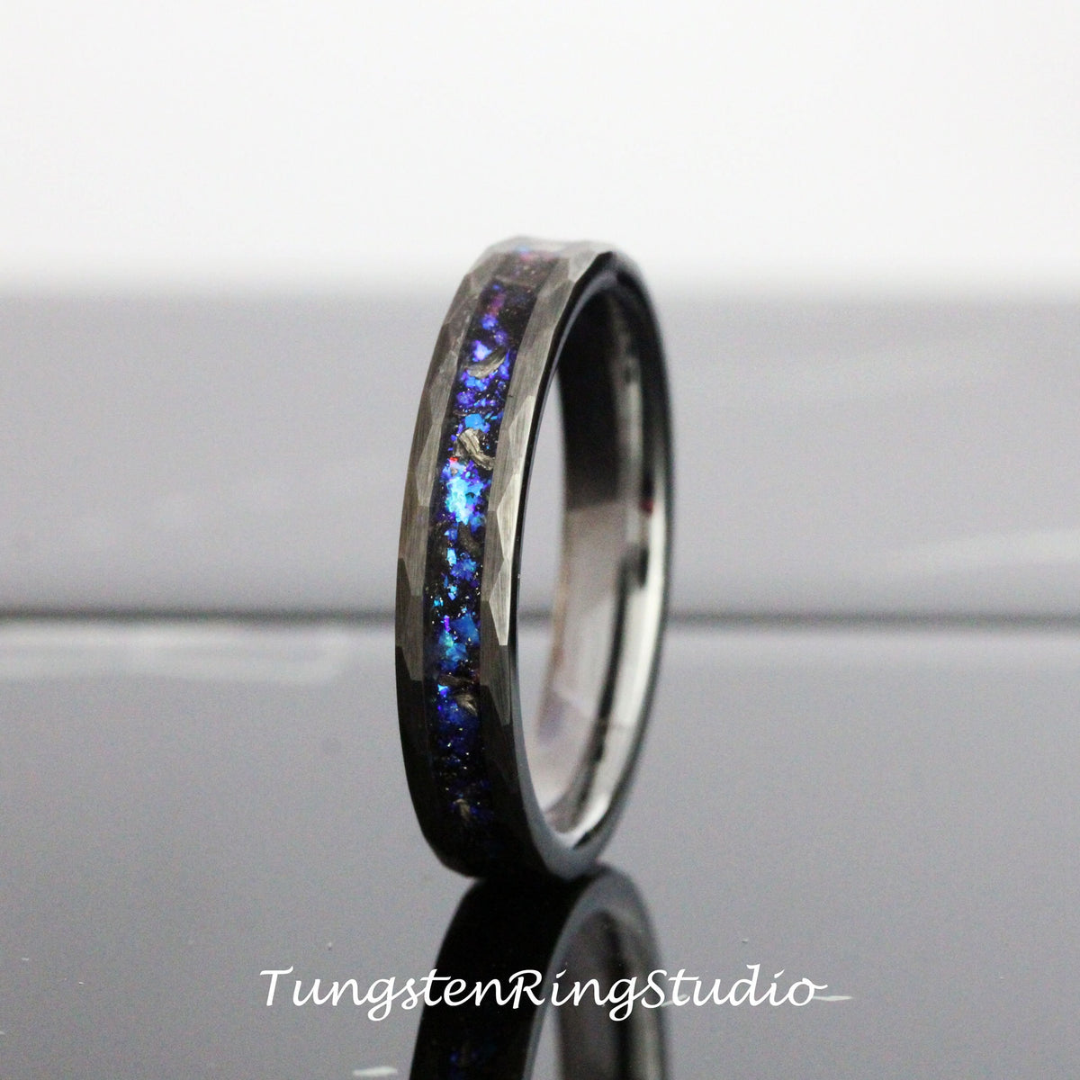 May include: A black tungsten carbide ring with a hammered finish and a blue and purple iridescent inlay.