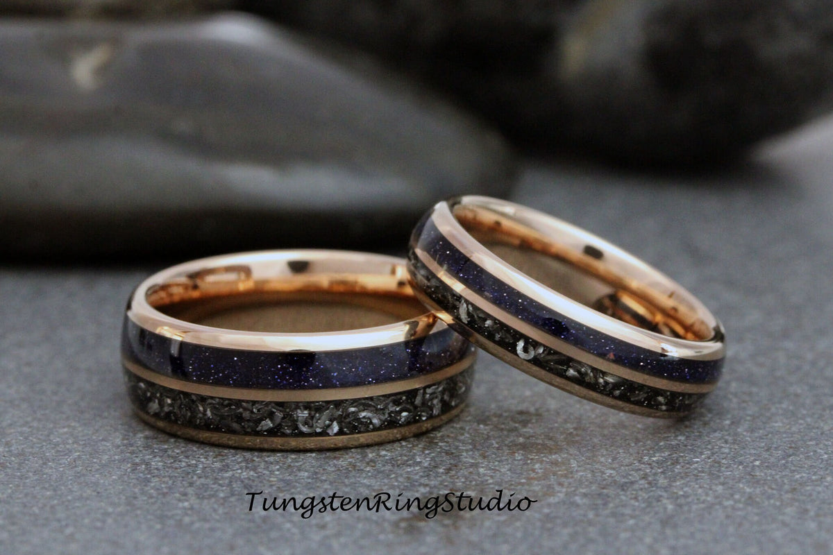 May include: Two matching wedding bands with a rose gold finish. The bands have a dark blue inlay with a thin silver band around the edge.