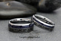 May include: Two matching rings with a silver band, a dark blue center, and a dark gray patterned inlay. The rings are displayed on a gray surface. The text "TungstenRingStudio" is visible at the bottom.