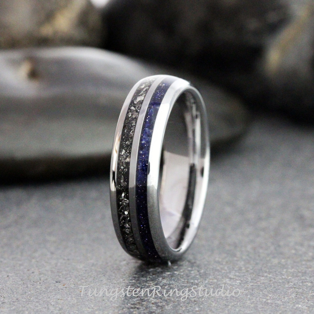 May include: A silver-colored ring with a dark gray center band and a vibrant blue band. The ring has a polished finish and the text "TungstenRingstudio" is visible at the bottom.