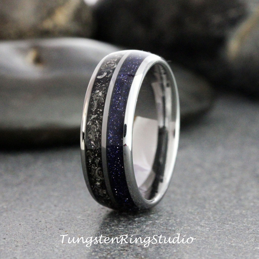 May include: A close-up of a silver ring with a dark blue, speckled center band and a black, textured band. The ring has a polished, metallic finish. The text "TungstenRingStudio" is at the bottom.