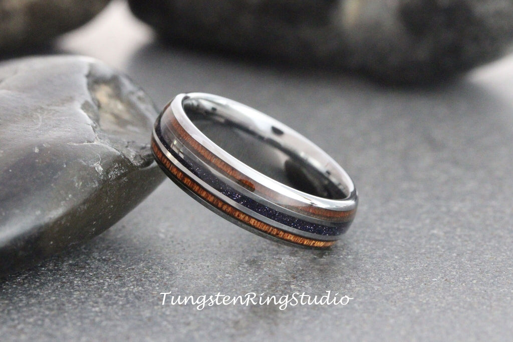 May include: A silver tungsten ring with a dark blue and brown wood inlay. The ring is on a gray background.