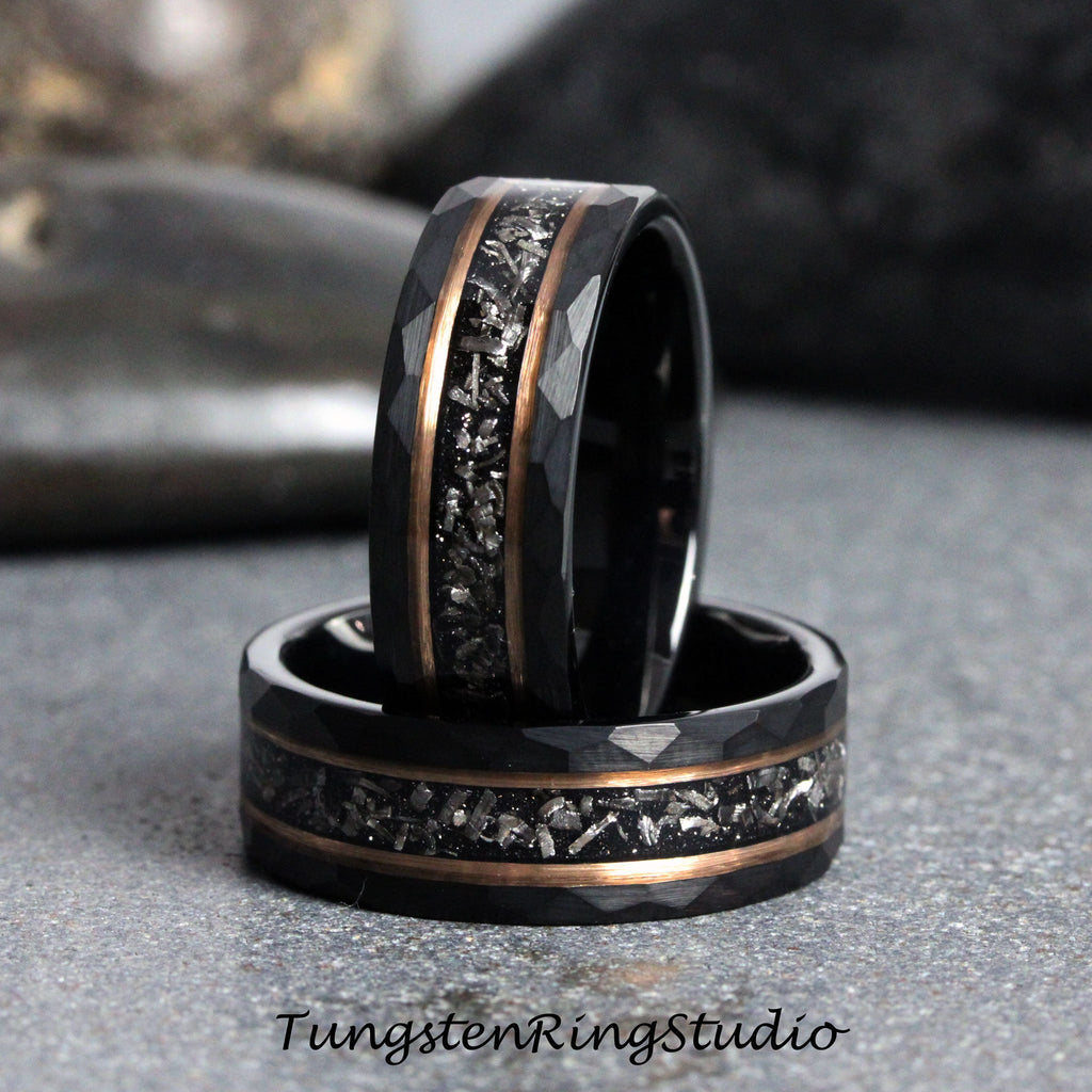 May include: Two black tungsten carbide rings with a hammered finish and a rose gold inlay. The inlay features a scattered pattern of small, silver-colored particles.