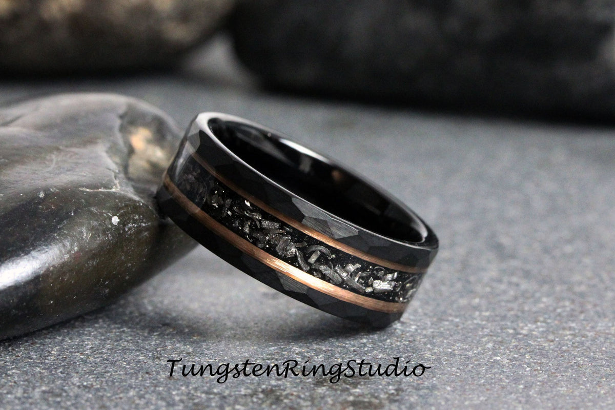May include: Black tungsten carbide ring with a hammered finish and a rose gold inlay. The inlay features a pattern of small, silver-colored particles.