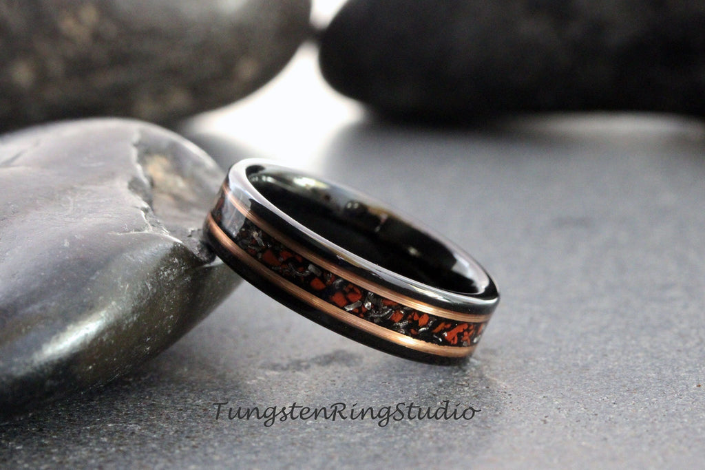 May include: A black tungsten ring with a copper inlay and a red and black speckled design. Tungsten Ring Studio is printed below the ring.