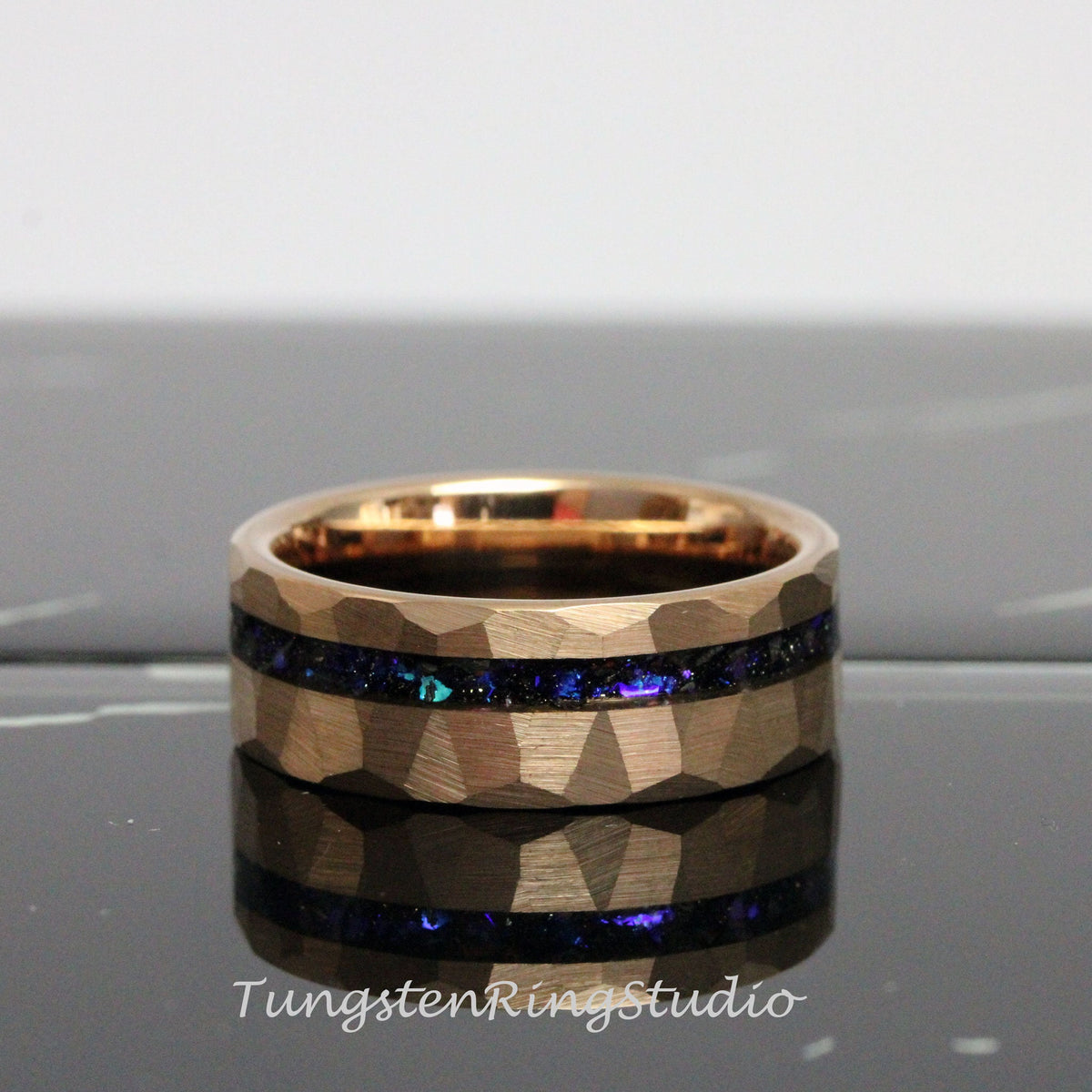 May include: A rose gold tungsten carbide ring with a hammered finish and a blue and purple inlay. The ring is approximately 8mm wide.