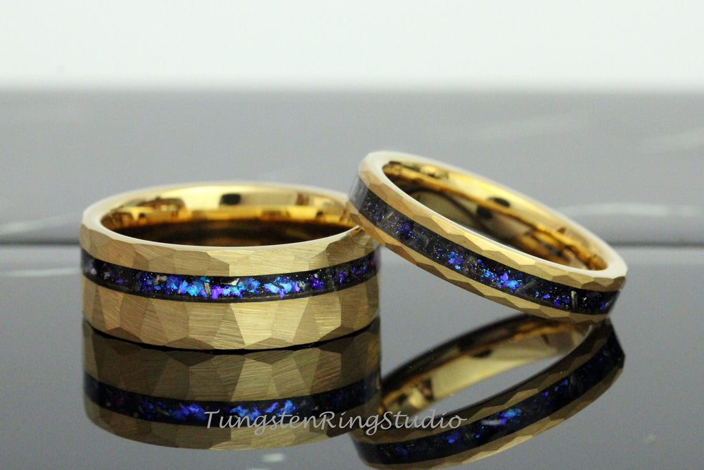 May include: Two gold tungsten carbide rings with a hammered finish and a blue and purple inlay. The rings are stacked on top of each other.