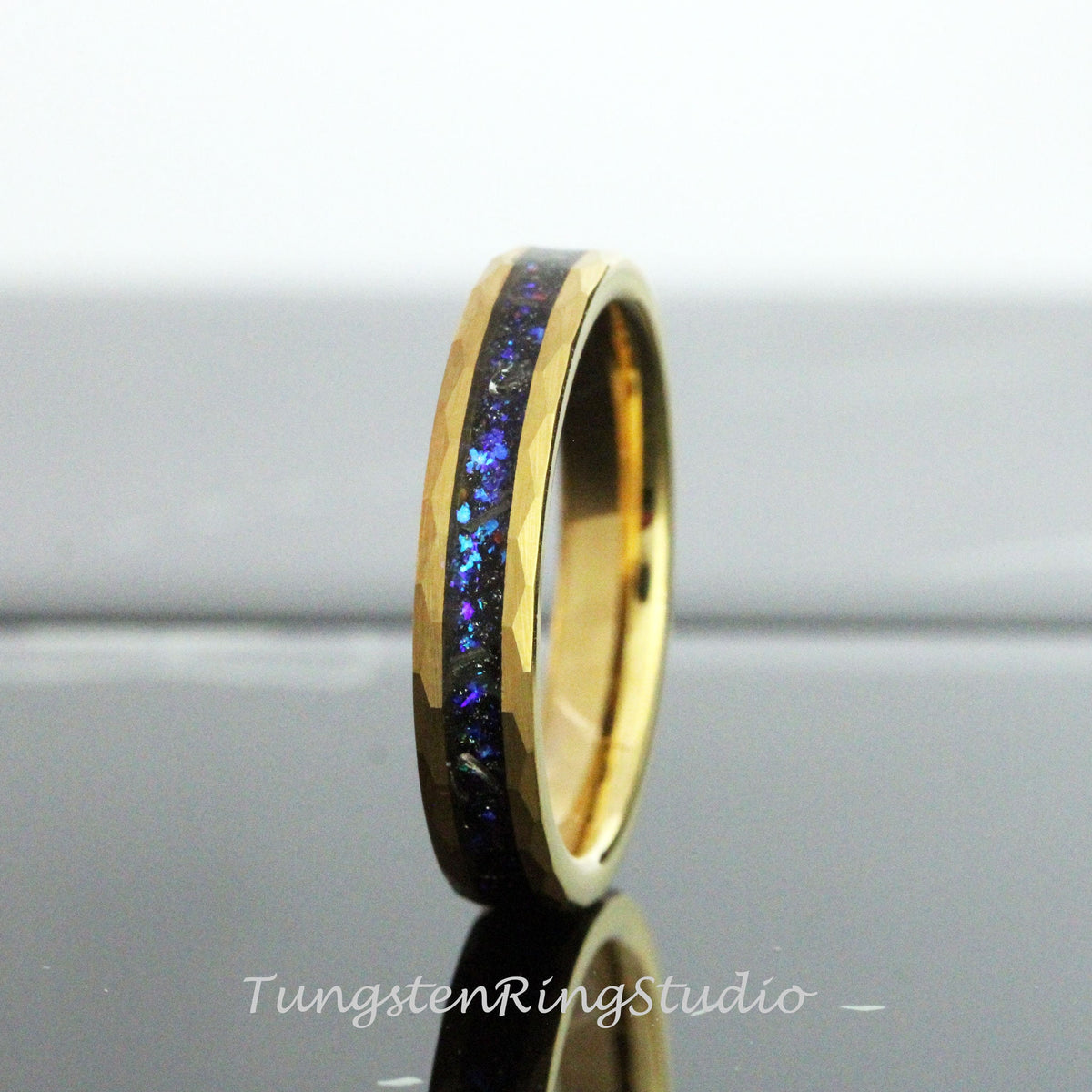 May include: A gold tungsten carbide ring with a black and blue inlay. The ring has a beveled edge and a brushed finish.