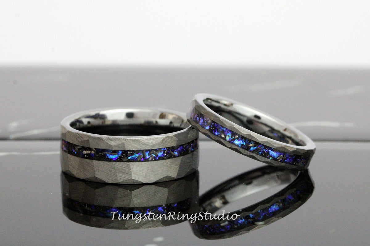 May include: Two tungsten carbide wedding bands with a hammered finish. One band features a blue and black inlay, while the other band has a blue inlay. The bands are on a white surface.