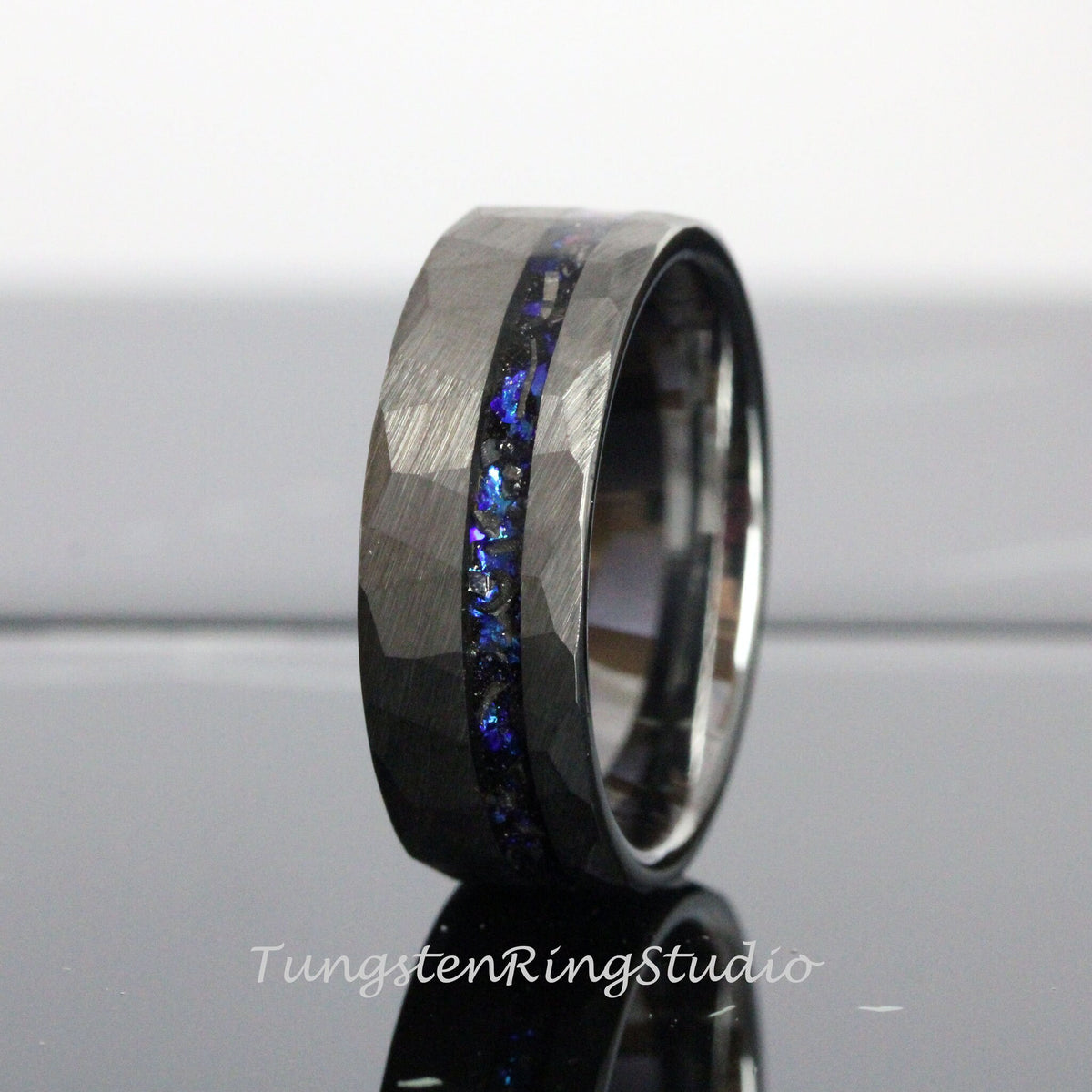 May include: A black tungsten carbide ring with a hammered finish and a blue and black inlay. The ring is a popular choice for men's wedding bands.