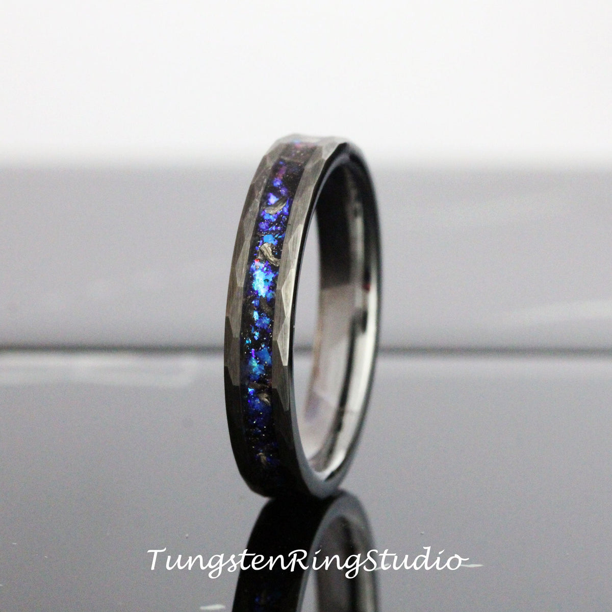 May include: A black tungsten carbide ring with a hammered finish and a blue and purple iridescent inlay.