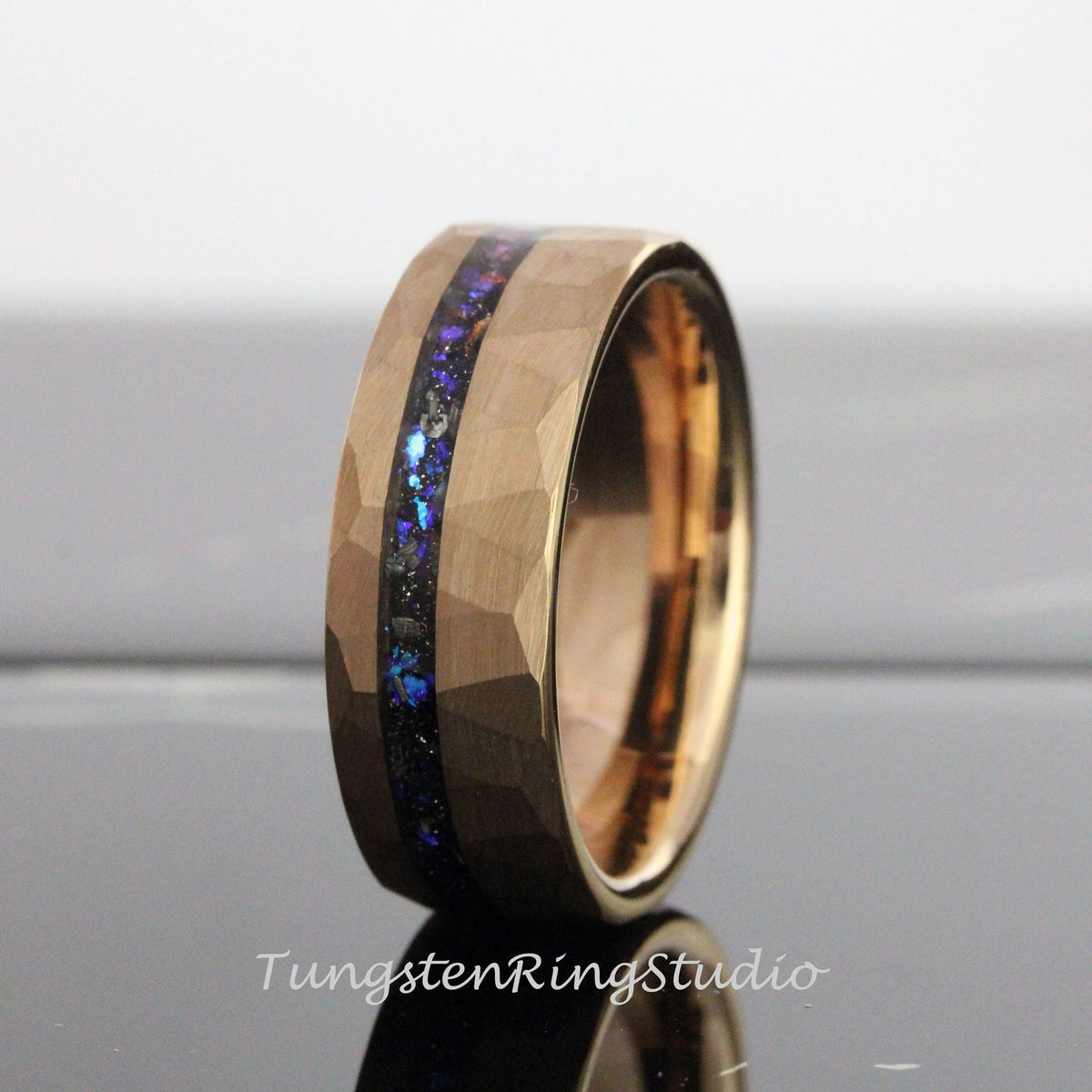 May include: A gold tungsten carbide ring with a hammered finish and a blue and black inlay. The ring is approximately 8mm wide.