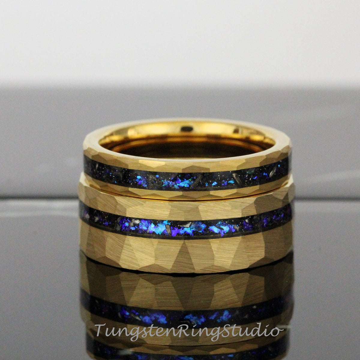 May include: Two gold tungsten carbide rings with a hammered finish and a blue and black inlay. The rings are stacked on top of each other.