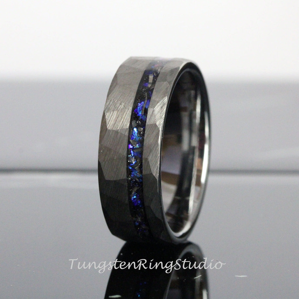 May include: A black tungsten carbide ring with a hammered finish and a blue and black inlay. The ring is a popular choice for men's wedding bands.