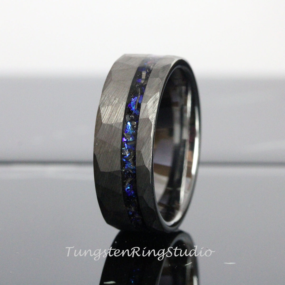 May include: A black tungsten carbide ring with a hammered finish and a blue and black inlay. The ring is a popular choice for men's wedding bands.