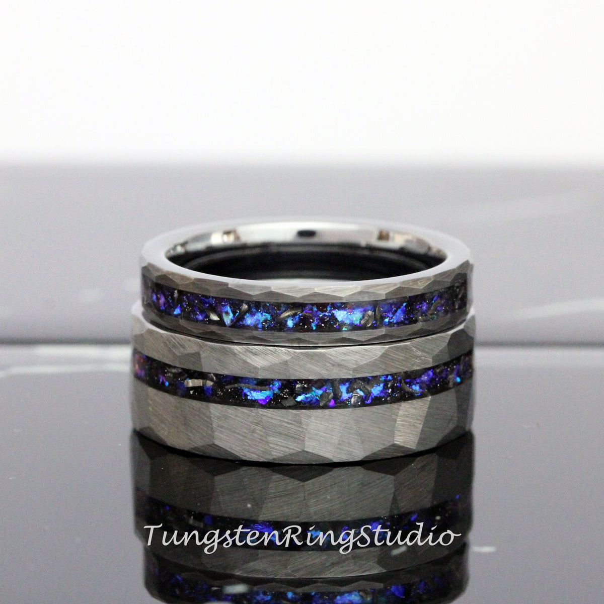 May include: Two silver tungsten carbide rings with a hammered finish and a blue and black inlay. The rings are stacked on top of each other.