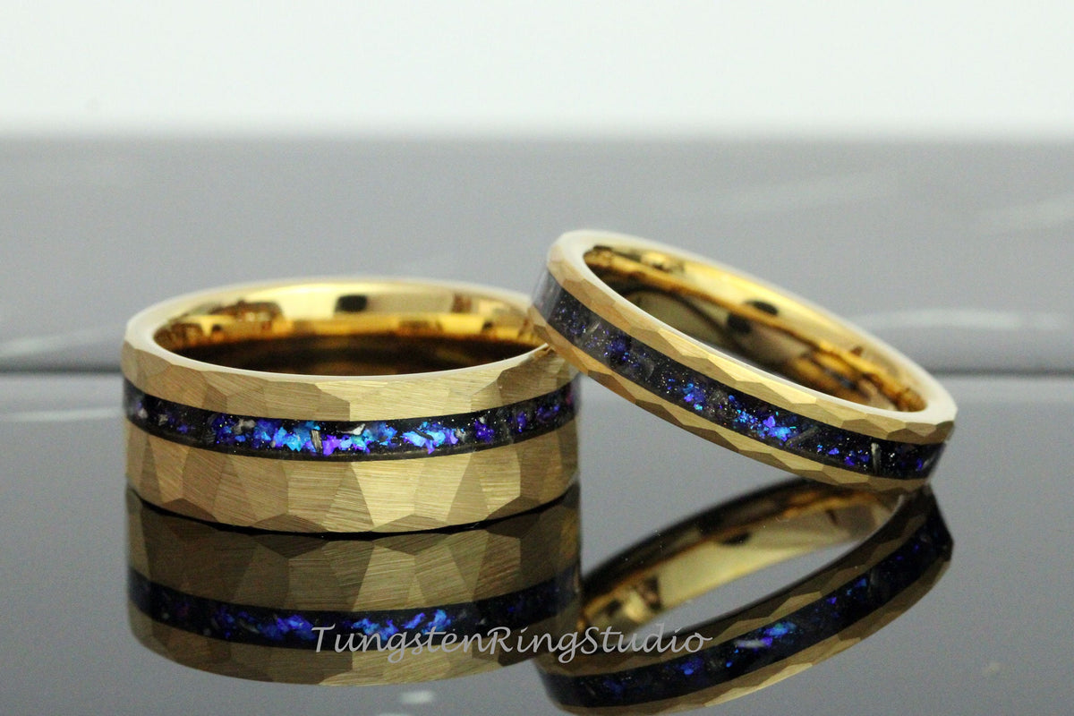 May include: Two gold tungsten carbide rings with a hammered finish and a blue and purple inlay. The rings are stacked on top of each other.