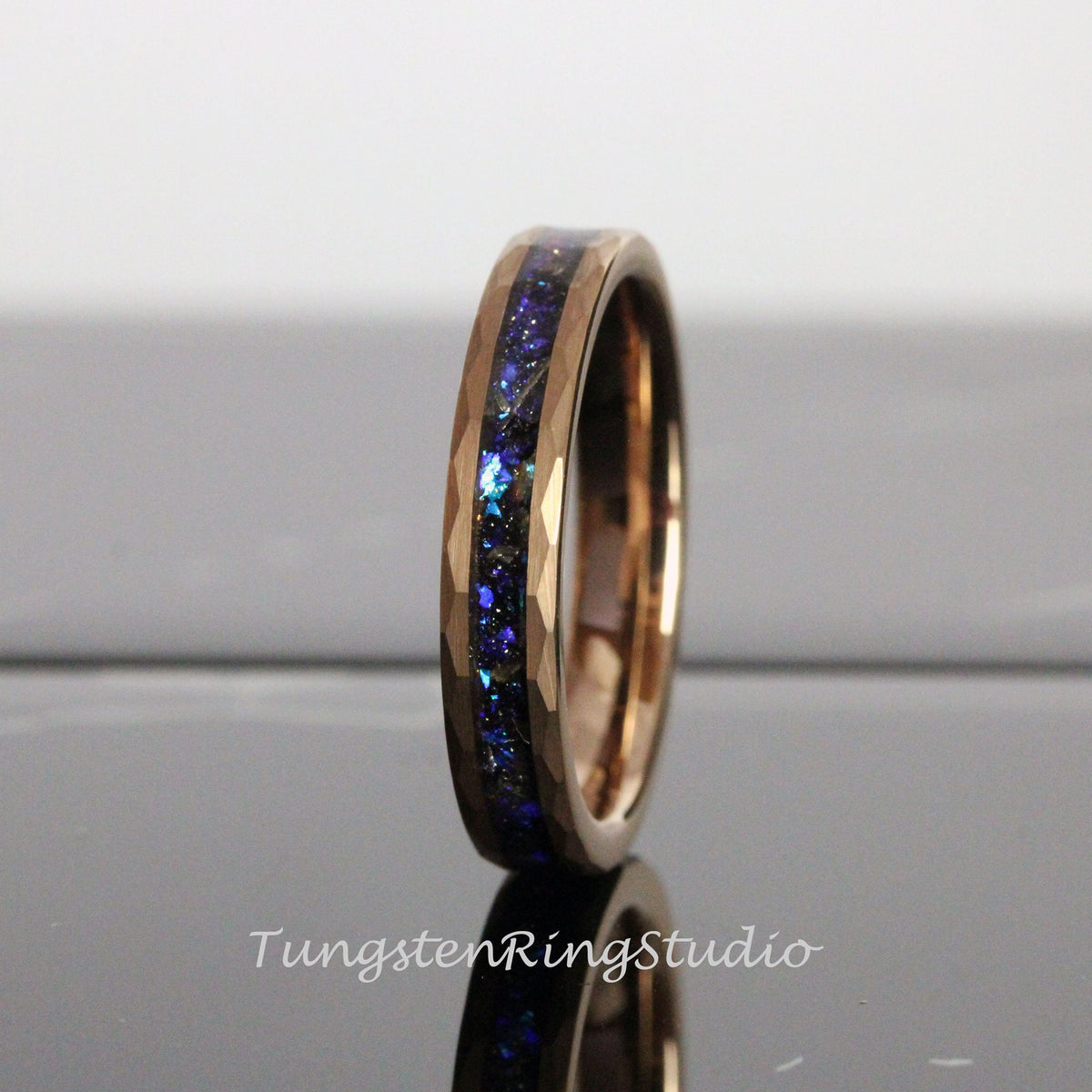 May include: A rose gold tungsten carbide ring with a blue and black inlay. The ring has a beveled edge and a polished finish.