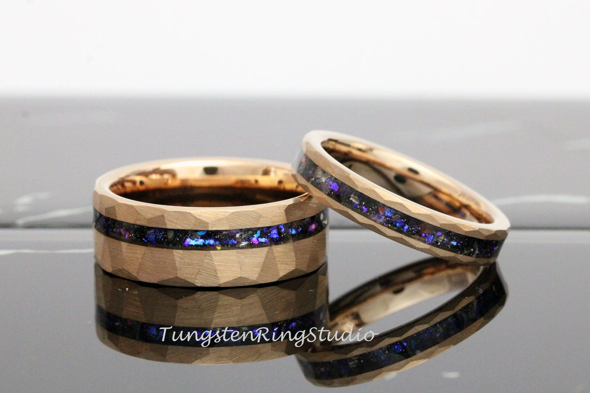 May include: Two gold tungsten carbide wedding bands with a hammered finish and a black inlay with iridescent blue and purple glitter.