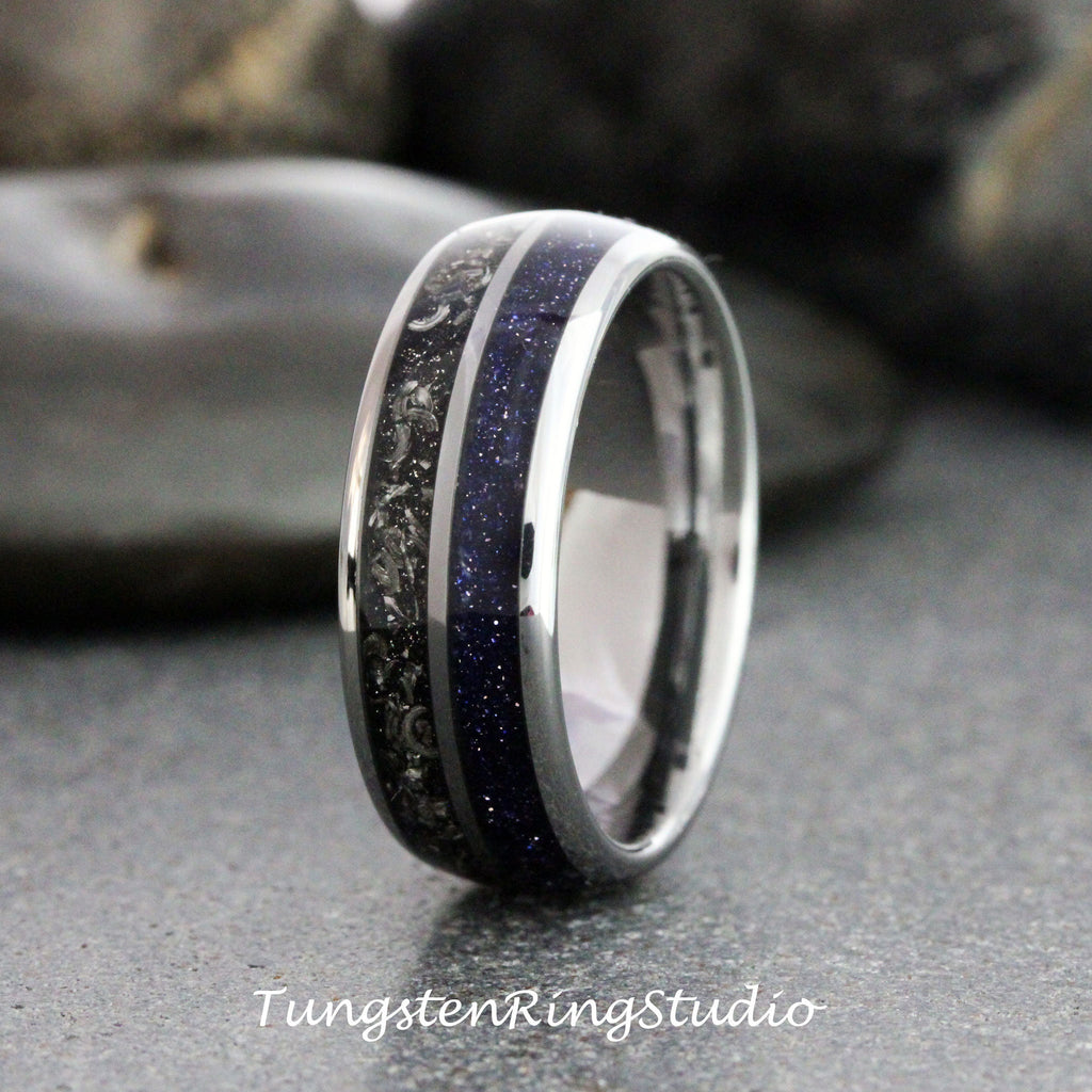 May include: A close-up of a silver ring with a dark blue, speckled center band and a black, textured band. The ring has a polished, metallic finish. The text "TungstenRingStudio" is at the bottom.