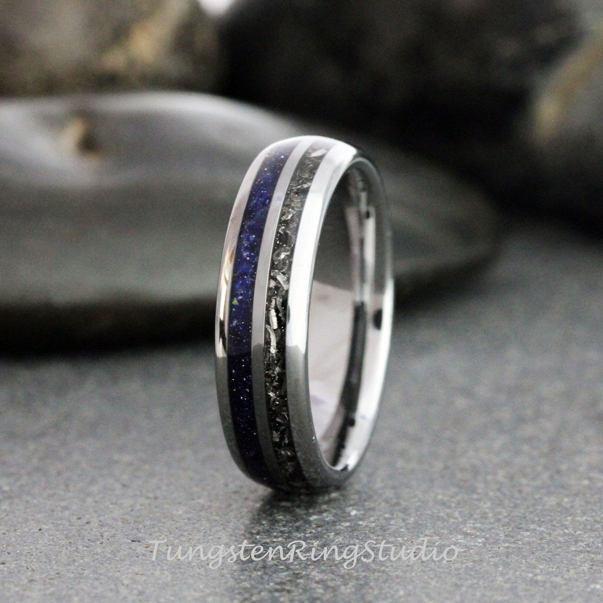 May include: A polished silver ring with a central band of dark blue and black speckled material. The ring has a smooth, reflective surface and a modern design. The text "TungstenRingStudio" is visible.