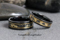 May include: Two black tungsten carbide rings with a gold inlay. The rings have a thin gold band with small gold flakes embedded in the black surface.