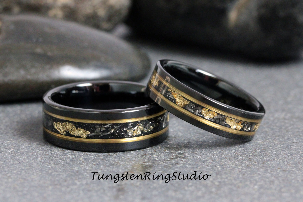May include: Two black tungsten carbide rings with a gold inlay. The rings have a thin gold band with small gold flakes embedded in the black surface.