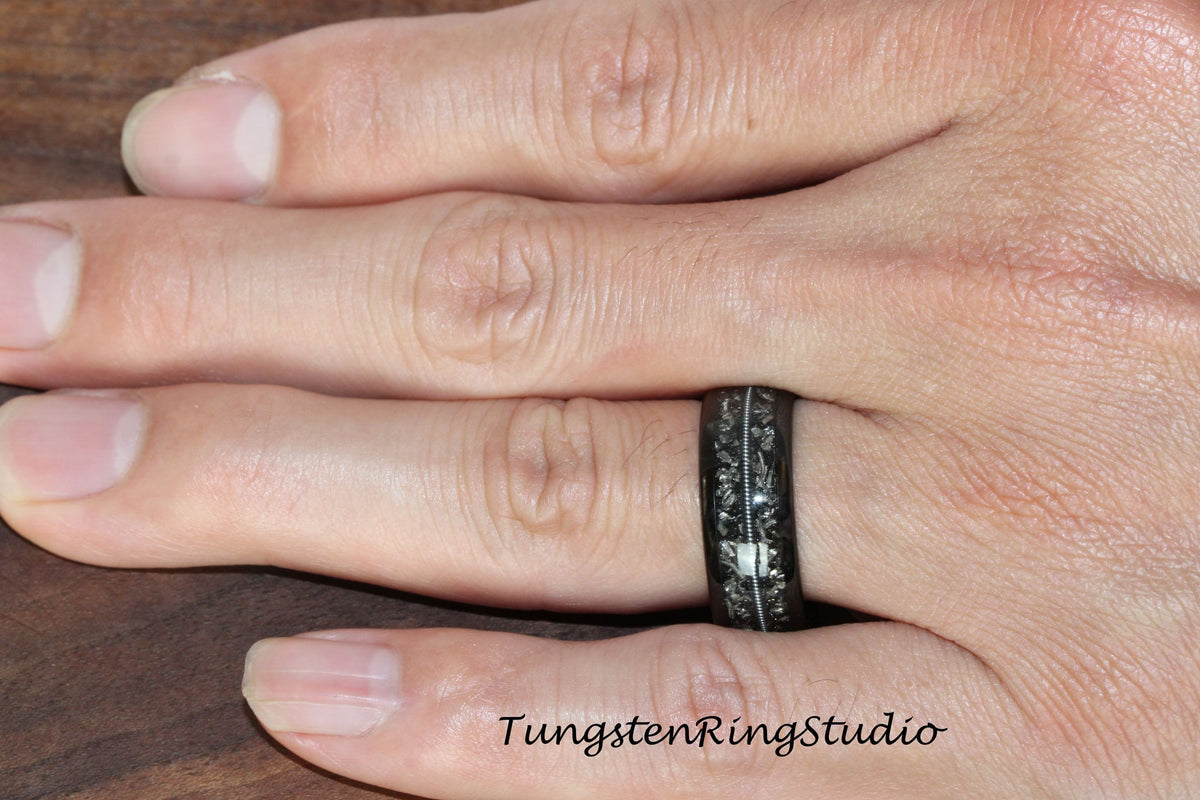 May include: A black tungsten ring with a silver inlay design. The ring is worn on a person's finger.