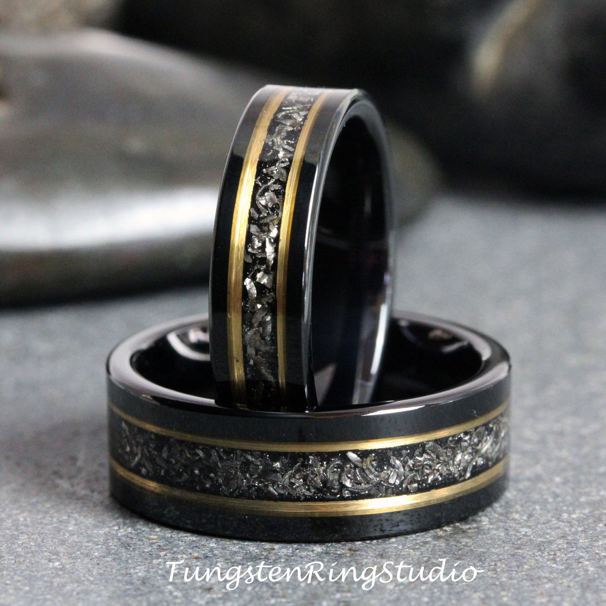 May include: Two black tungsten carbide rings with gold inlay and a silver-grey speckled pattern. The rings are stacked on top of each other.